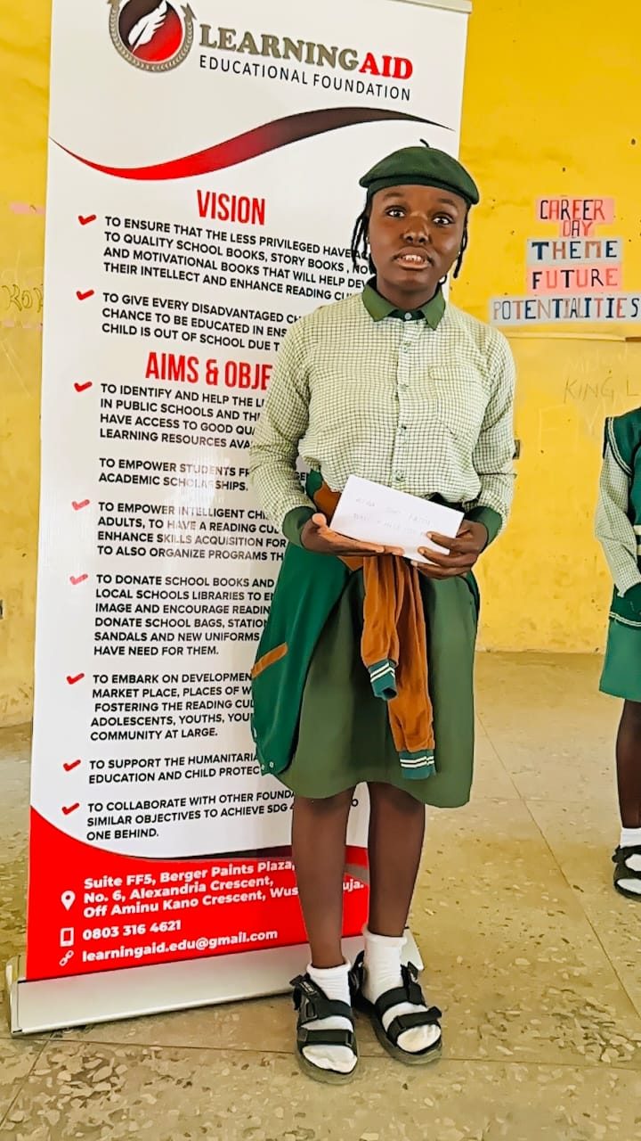 An SS3 student holding her WAEC support envelope beside the LEF banner.